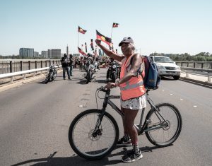 An Indigenous woman stands on a bridge waving the Aboriginal flag