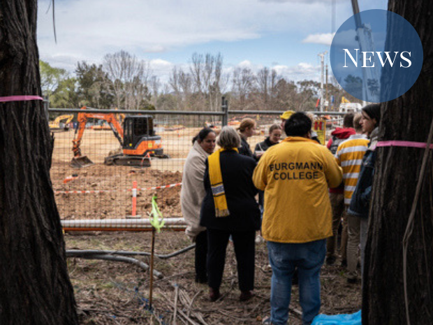 Students and staff in Burgmann merchandise gather near the fence near the construction site